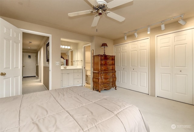 carpeted bedroom with two closets, ensuite bath, ceiling fan, and track lighting