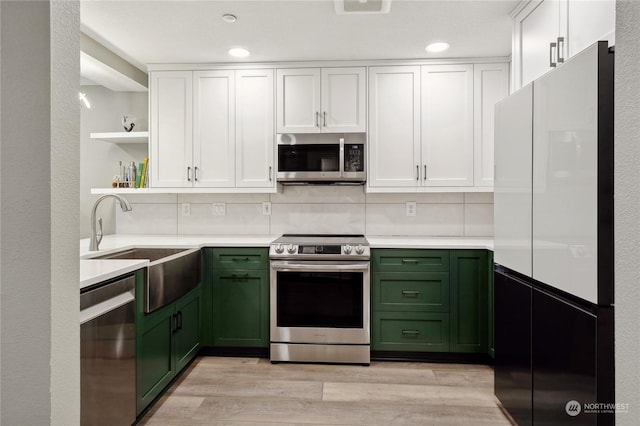 kitchen featuring white cabinetry, sink, light hardwood / wood-style floors, green cabinetry, and stainless steel appliances