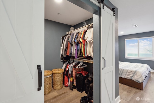 walk in closet with a barn door and light hardwood / wood-style flooring