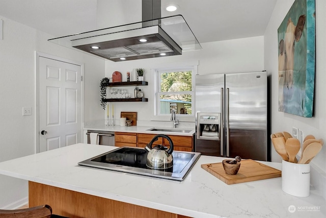 kitchen with island exhaust hood, appliances with stainless steel finishes, light stone countertops, and sink