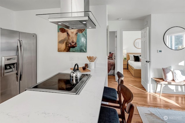 kitchen featuring stainless steel fridge, island exhaust hood, black electric stovetop, kitchen peninsula, and light hardwood / wood-style flooring