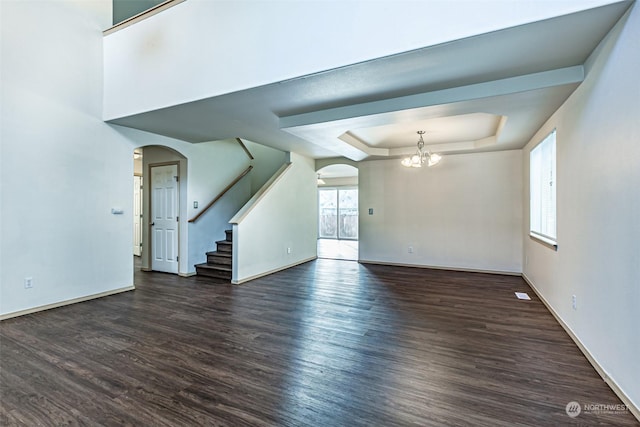 empty room with a raised ceiling, an inviting chandelier, and dark hardwood / wood-style flooring