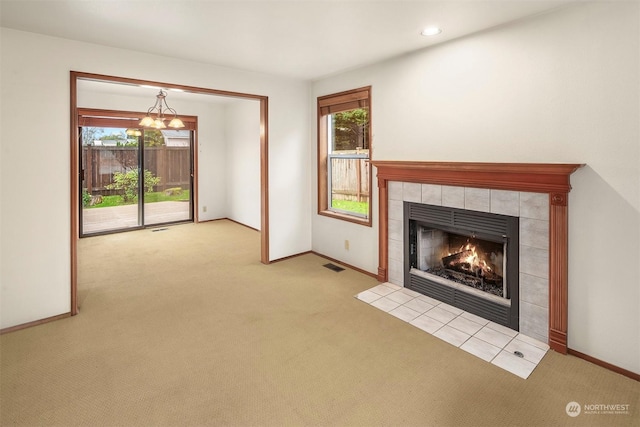 unfurnished living room with a tiled fireplace, light colored carpet, and a chandelier