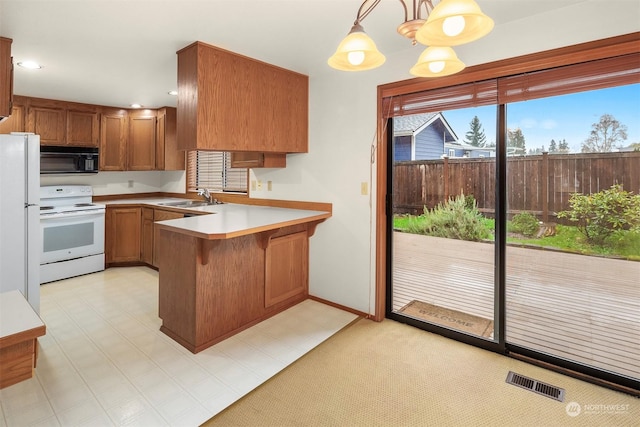 kitchen featuring sink, white appliances, hanging light fixtures, a kitchen bar, and kitchen peninsula