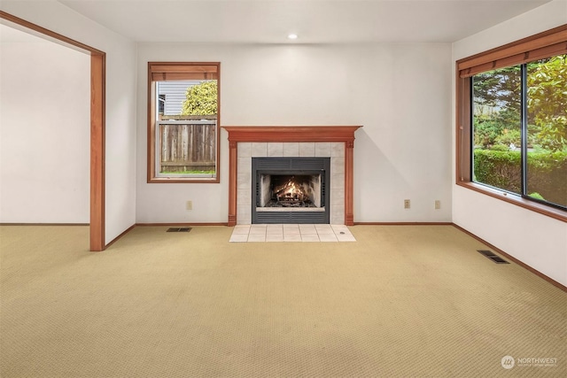 unfurnished living room with a tiled fireplace, a healthy amount of sunlight, and carpet floors