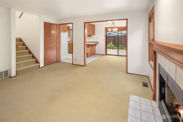 unfurnished living room with a tile fireplace, light carpet, and a chandelier