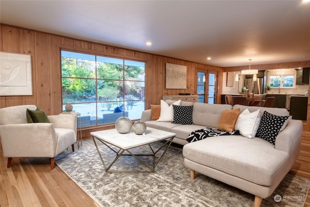 living room featuring french doors, plenty of natural light, light hardwood / wood-style flooring, and wood walls