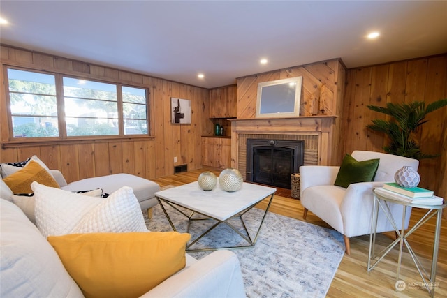 living room with a brick fireplace, light hardwood / wood-style floors, and wood walls