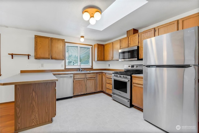 kitchen featuring appliances with stainless steel finishes, sink, kitchen peninsula, and a skylight