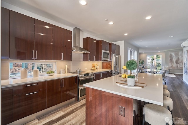 kitchen featuring wall chimney range hood, a breakfast bar, hardwood / wood-style floors, stainless steel appliances, and a center island