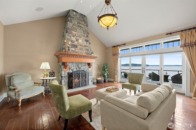 living area featuring hardwood / wood-style floors, baseboards, high vaulted ceiling, a stone fireplace, and a water view