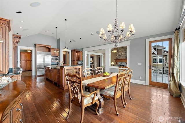 dining area with dark wood finished floors, a stone fireplace, lofted ceiling, and decorative columns