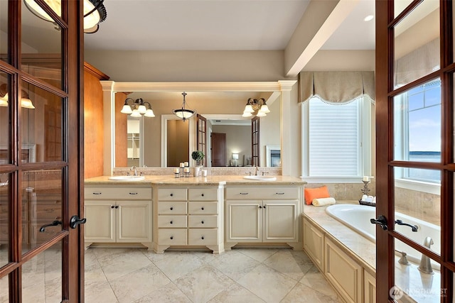 bathroom featuring double vanity, french doors, a garden tub, and a sink