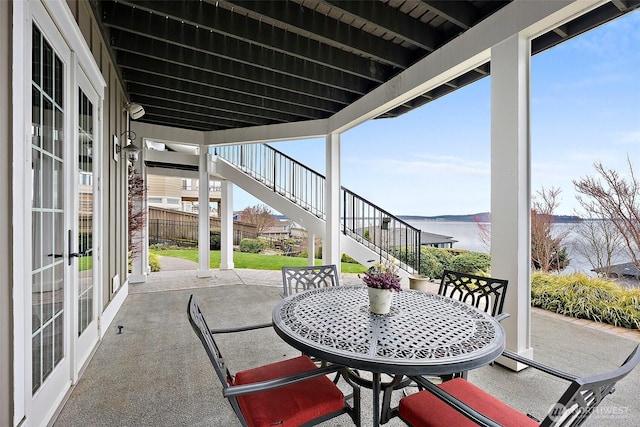 view of patio featuring stairway, outdoor dining area, fence, and a water view