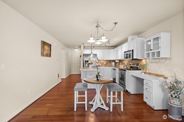 kitchen featuring white cabinetry, backsplash, stainless steel appliances, a kitchen bar, and decorative light fixtures