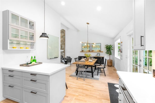 kitchen with light wood-type flooring, lofted ceiling, hanging light fixtures, a breakfast bar, and an inviting chandelier