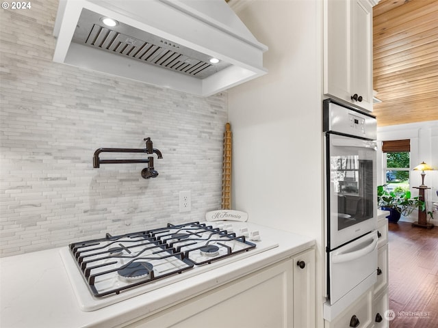 kitchen with white cabinetry, backsplash, dark wood-type flooring, custom range hood, and white appliances