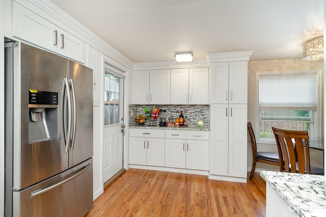 kitchen with white cabinetry, backsplash, stainless steel fridge, light stone counters, and light wood-type flooring