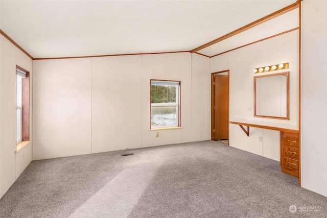 carpeted empty room featuring crown molding, built in desk, and vaulted ceiling