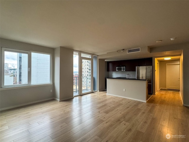 unfurnished living room featuring expansive windows, sink, and light hardwood / wood-style flooring