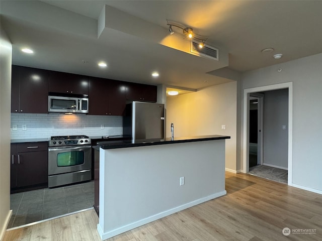 kitchen featuring sink, light hardwood / wood-style flooring, appliances with stainless steel finishes, a kitchen island with sink, and tasteful backsplash