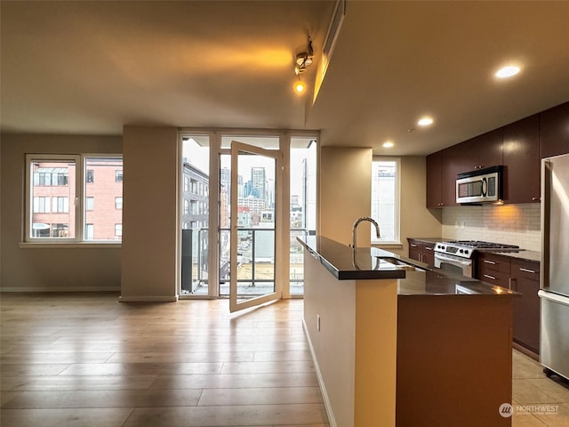 kitchen featuring appliances with stainless steel finishes, an island with sink, dark brown cabinets, and backsplash