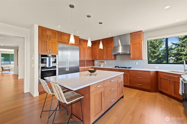 kitchen with wall chimney exhaust hood, sink, hanging light fixtures, appliances with stainless steel finishes, and a kitchen island