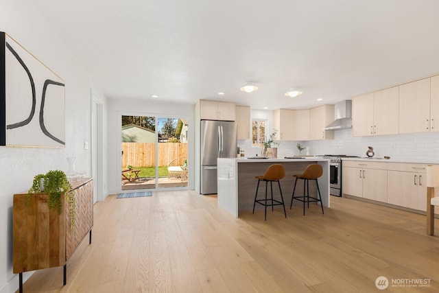 kitchen featuring wall chimney range hood, a center island, appliances with stainless steel finishes, a breakfast bar area, and light wood finished floors