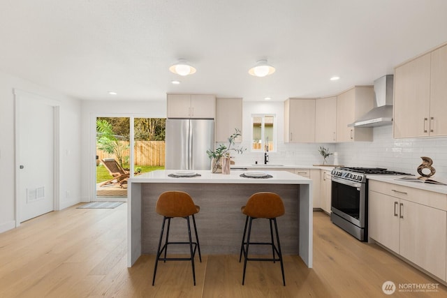 kitchen with a kitchen bar, backsplash, a kitchen island, stainless steel appliances, and wall chimney exhaust hood