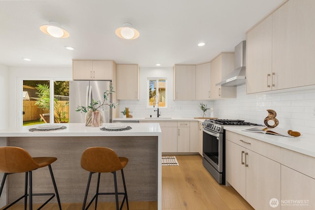 kitchen featuring wall chimney range hood, a breakfast bar area, a wealth of natural light, appliances with stainless steel finishes, and a sink