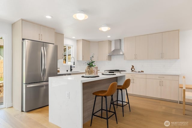 kitchen featuring a healthy amount of sunlight, freestanding refrigerator, wall chimney range hood, and a sink