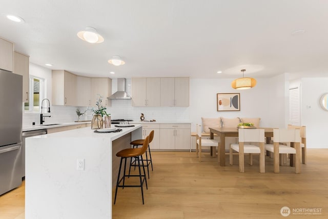 kitchen with wall chimney range hood, light countertops, a kitchen breakfast bar, freestanding refrigerator, and a sink