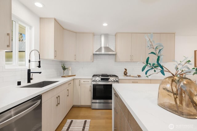 kitchen featuring light wood-type flooring, a sink, wall chimney range hood, appliances with stainless steel finishes, and light countertops