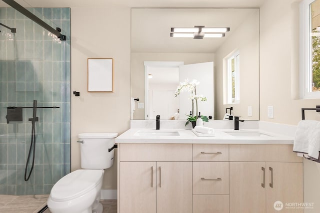 full bath with a sink, toilet, a stall shower, and double vanity