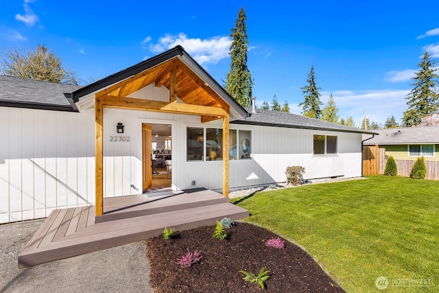 back of property with a lawn, fence, and a shingled roof