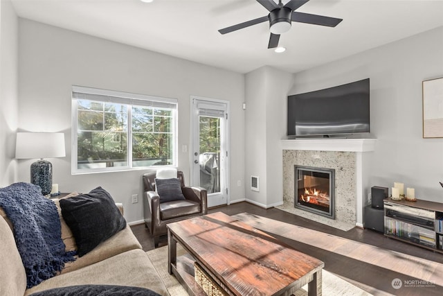 living room featuring dark wood-type flooring, a premium fireplace, and ceiling fan