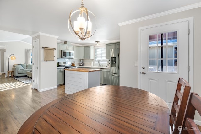 dining area with an inviting chandelier, ornamental molding, sink, and light wood-type flooring