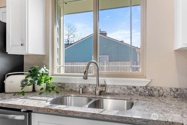 kitchen with white cabinetry, sink, light stone counters, and stainless steel dishwasher