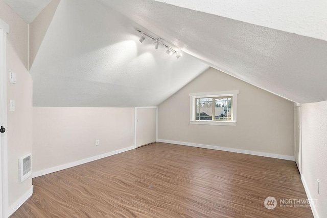 additional living space featuring hardwood / wood-style flooring, vaulted ceiling, and a textured ceiling