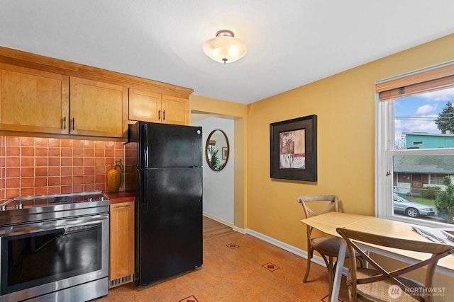 kitchen with electric range, baseboards, dark countertops, freestanding refrigerator, and backsplash