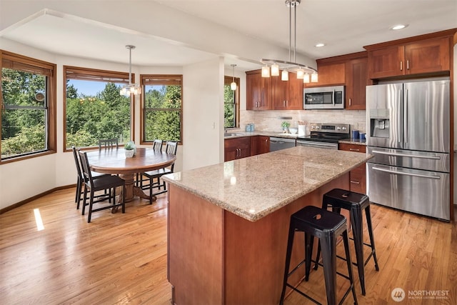 kitchen with a kitchen island, appliances with stainless steel finishes, decorative light fixtures, light hardwood / wood-style floors, and light stone countertops