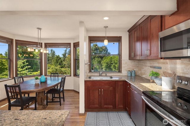 kitchen featuring stainless steel appliances, sink, light stone counters, and decorative light fixtures