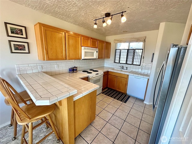 kitchen with tile countertops, light tile patterned floors, tasteful backsplash, white appliances, and a peninsula