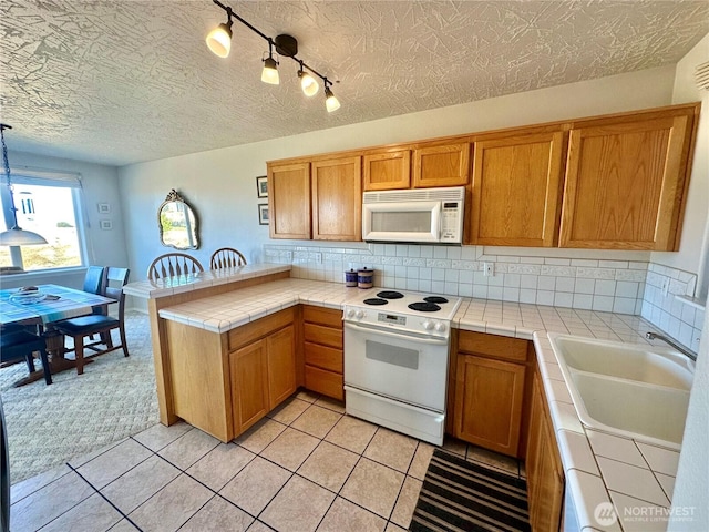 kitchen featuring tile counters, decorative backsplash, a sink, white appliances, and a peninsula