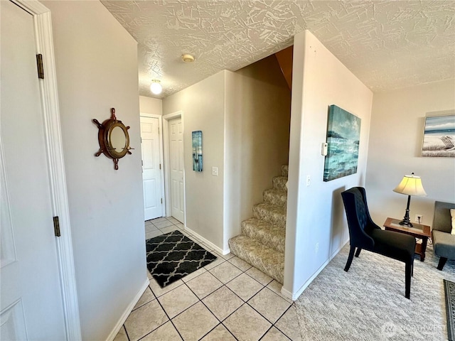 foyer entrance with a textured ceiling, light tile patterned floors, and baseboards