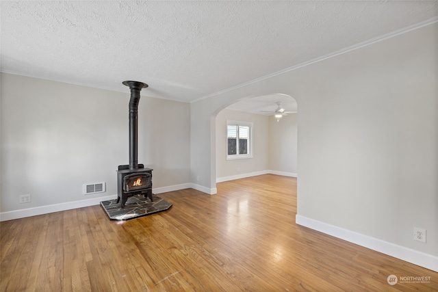 unfurnished living room with ornamental molding, light hardwood / wood-style floors, a textured ceiling, and a wood stove