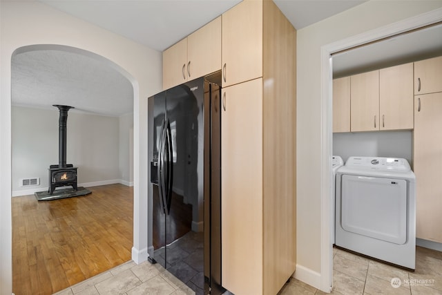 kitchen featuring cream cabinets, black fridge with ice dispenser, a textured ceiling, and a wood stove