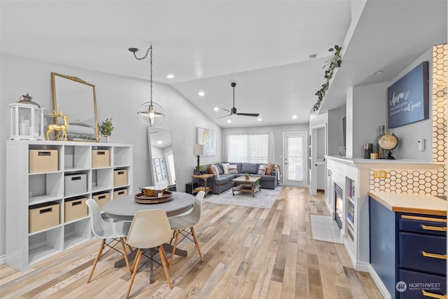 dining room with ceiling fan, lofted ceiling, light hardwood / wood-style floors, and a tile fireplace