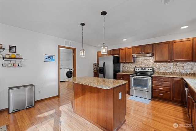 kitchen featuring a kitchen island, washer and dryer, pendant lighting, stainless steel appliances, and light wood-type flooring