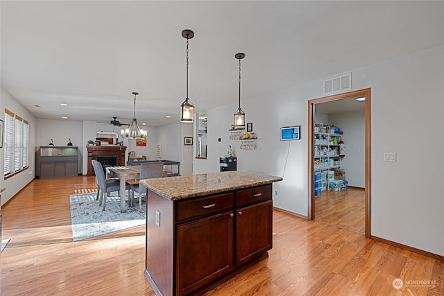 kitchen with light hardwood / wood-style floors, decorative light fixtures, light stone countertops, and a center island